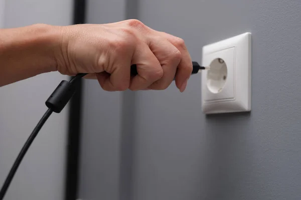 Woman hand inserts electrical plug into outlet closeup — Stock Photo, Image
