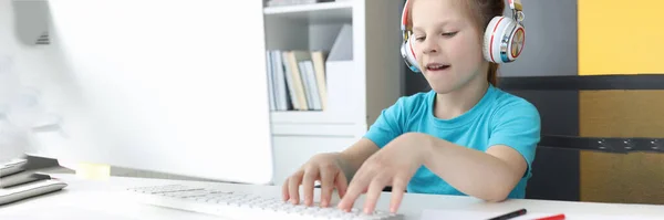 Chica en auriculares se sienta en el monitor de la computadora y los tipos en el teclado —  Fotos de Stock