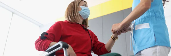 Koruyucu tıbbi maskeli doktor fizyoterapist klinikte engelli bir hastanın elini tutuyor. — Stok fotoğraf