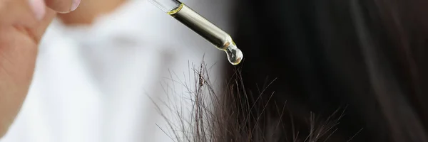 Donna che gocciola olio giallo dalla pipetta sulle doppie punte del primo piano dei capelli — Foto Stock