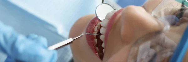Dentysta w rękawiczkach ochronnych badający zęby pacjentki za pomocą metalowych przyrządów w klinice zbliżenie — Zdjęcie stockowe
