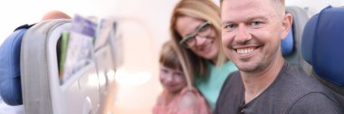 Aile babası anne kızı uçakta oturuyor ve gülümsüyor.
