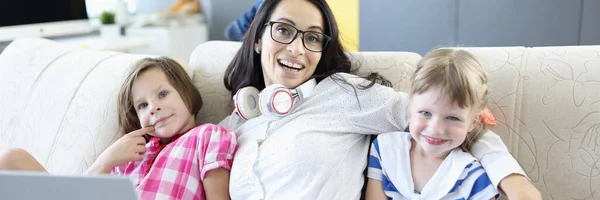 Mujer sonriente sentada con portátil y niños en el sofá. — Foto de Stock