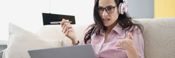 Mulher irritada em óculos e fones de ouvido sentados na frente do monitor do laptop com documentos em casa — Fotografia de Stock