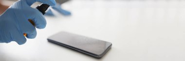 Eldivenli kişi akıllı telefonu dezenfektanla kapatır.