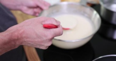 Adam tencere ve yağ şişesinin yanındaki tezgahta karıştırma kabını tutuyor. Fırıncı kepçeyi çevirir ve karıştırır. Hamur, pürüzsüz döküm hazırlarken topakları kaldırır.