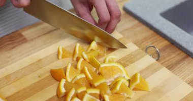 Kişi, tahta kesme tahtasıyla turuncu kesiyor. Keskin bir bıçak ve sabit bir elle. Aşçı parçaları hazırlamak için yana kaydırırken bıçakları ayırıyor.