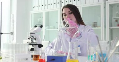 Kadın laboratuvar asistanı, laboratuarda çalışan Erlenmeyer şişesine temiz su döküyor. Kadın araştırmacı sıvı kalitesini test ekipmanlarıyla kontrol ediyor