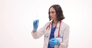 Odaklanmış kadın doktor beyaz arka planda aşıyla şırınga tutuyor. Esmer kadın doktor randevusunda hastaya iğne yapmaya hazırlanıyor.