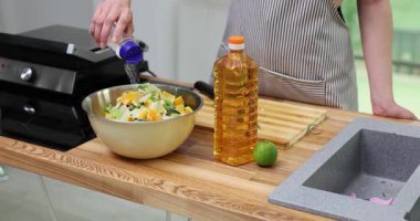 Kadın şef, doğranmış sebzelere yağ şişesinin yanındaki karıştırma kabında tuz ekliyor. Aşçı sallar, kristalleri serper ve parçaları ağır çekimde fırlatır.