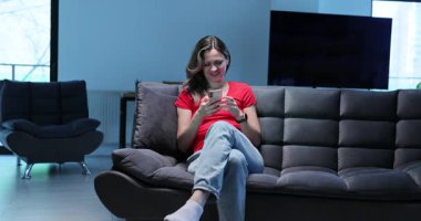 Kanepede bacak bacak bacak üstüne atmış, elinde akıllı telefon tutan bir kadın oturuyor. Kadın kullanıcı parşömenleri besleniyor ve kısa aralarda nazikçe gülümsüyor