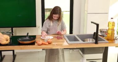 Ergen kızlar yemek yer ve prosciutto dilimlerini ahşap tezgaha koyar. Odaklanmış tatlı liseli kız mutfak stüdyosunda öğle yemeği için lezzetli etler hazırlıyor.