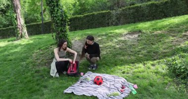 Kadın çantadan çalışma günlüklerini çıkarıp kız arkadaşına veriyor. Battaniye planında spor envanteri olan kadınlar açık havada birlikte egzersiz yapıyorlar.