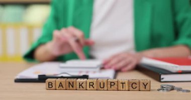 Hareketli bir ofiste, birisi iflası düşünürken notlar yazar. Sıcak ışık, önemli mali evrak ve düşüncelerine odaklandıklarını vurguluyor..