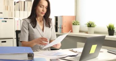 Ofisteki kadın elinde belge tutarken dirseğine hapşırıyor. İşçiler, ofiste çalışırken mikropların yayılmasını önlemek için burun ve ağızlarını doğru şekilde kapatırlar.