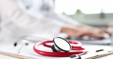 Kırmızı steteskop ve hasta tıbbi kayıtları tıp bürosundaki doktor masasında. Hastanedeki iş yerinde bilgisayar klavyesinde çalışan kadın hekim tipleri