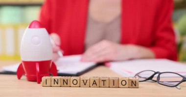 Parlak bir çalışma alanında, küçük bir roket modeli yenilikçi fikirleri sembolize ederken bir kişi notlara ve çizimlere odaklanır. Sıradan çalışma anları için bardaklar yakında dinleniyor..