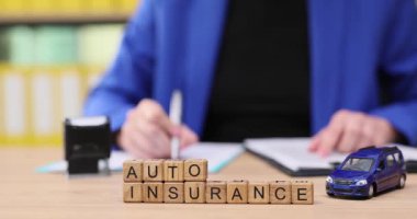 Parlak bir ofis ortamında, araba modelleri ve sigorta mektuplarıyla çevrili bir kişi notlar yazar. Otomobil sigortasının ve akıllı seçimlerin önemi etkinliklerinde vurgulanır.