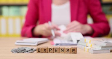 Sıcak bir ofis alanında, bir kişi faturaları düzenler ve bir hesap makinesi kullanarak giderleri hesaplar. Atmosfer odaklı ve sakin. Finansal planlamanın önemini vurguluyor..