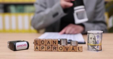 Parlak bir ofiste, bir kişi sevinçle kredi onayı belgelerini nakitle damgalar. Hevesle kredi onayını engelliyor, başarılarından dolayı mutluluğu yayıyorlar..