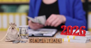 Bir kişi 2026 mali hedeflerini düşünürken parayı ve stratejik notları inceler. Aletler arasında nakit, sermaye sembolleri ve onlardan önce düzgünce düzenlenmiş planlama materyalleri yer alıyor.