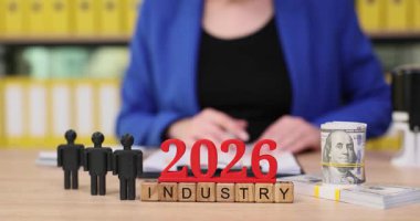 Aydınlık bir ofiste, insan 2026 'da endüstrinin geleceği için planlar tartışıyor. Tahta bloklar yıl ve endüstri temaları sergilerken, para birimi mali yönleri ön plana çıkarıyor.
