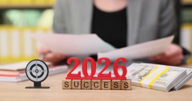 2026 sembol ve nakit destelerle süslenmiş bir masada bir kişi önemli belgeleri gözden geçirir. Atmosfer hırsı ve gelecekteki başarılara hazırlanmayı yansıtıyor..