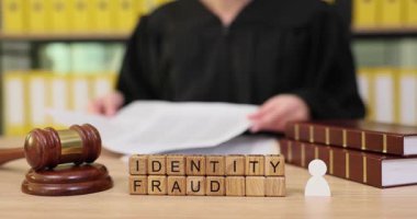 Yasal bir ortamda, yargıç kimlik sahtekarlığının karmaşıklığını ortaya çıkaran belgeleri inceler. Tahta bloklar terimi heceleyerek bu konunun önemini vurguluyor..