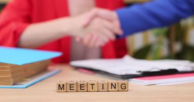 İki birey, üretken bir işbirliğini simgeleyen sıkı bir tokalaşma içinde. Belgeler ve renkli klasörler masanın üzerinde profesyonel bir atmosfer yaratacak şekilde düzenlenmiştir..