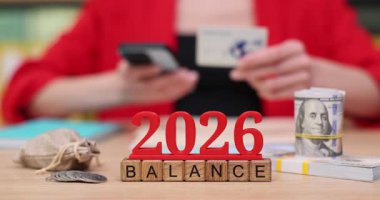 Eller, 2026 yılının finansal planlamasını tartışırken bir masada akıllı telefon ve objelerle aktif olarak iletişim kurarken görülüyor. Renkli yerleşim ilham verici elementler ve araçlar içerir.