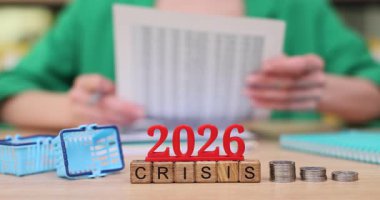 Bir kişi, 2026 mali krizini yansıtan madeni paralar ve hesap makinesiyle çevrelenmiş önemli belgeleri analiz eder. Odaklanmış ifadeleri, planlamanın aciliyetini vurgular..
