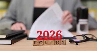 Odaklanmış bir profesyonel, 2026 'nın kilit politikalarını vurgulayan önemli belgeleri masa başında inceler. Kağıtlar ve araçlar düzgünce düzenlenir, organizasyon vurgulanır ve yaklaşan değişikliklere hazırlık yapılır.