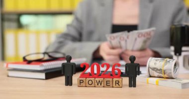 Eller nakit ve banknotları gösteriyor, finansal gücü simgeliyor. Bir tablo planlama ve büyüme araçlarını gösterir, 2026 'ya odaklanır ve güçlendirme.