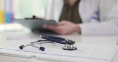 Kadın doktor masada oturuyor ve hasta için detaylı tedavi planı yazıyor. Doktor randevudaki tedavi aşamalarını kaydediyor. Yavaş çekim