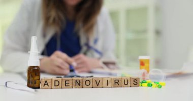 Kadın doktor, Adenovirüs yakınlarında tahta bloklar ve masa başındaki burun spreyi şişesiyle ilgili kağıtları inceliyor. Viral enfeksiyonların adenovirüs teşhisine odaklanın