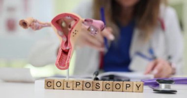 Doktor Colposcopy yakınlarında tahta bloklar ve üreme sistemi modeli üzerine reçete yazıyor. Jinekolojik muayene ve teşhisi