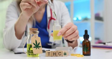 Küpler, esrar bileşik araştırmasına atıfta bulunan THC sözcüğünü gösteriyor. Doktor elinde damla olan küçük şişe ve sıvı örnekleri tıbbi temayı destekliyor