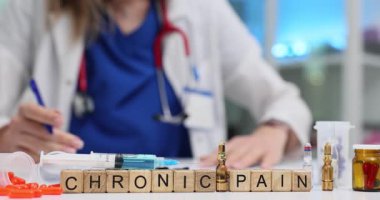 Küpler, Kronik Ağrı 'nın uzun vadeli sağlık sorununu vurguladığını söyler. Masadaki haplar ve şırıngalar sürekli rahatsızlık veren tıbbi mücadeleyi vurguluyor