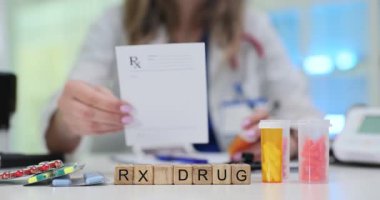 Tahta küplere göre ilaç sözcüğü laboratuvar masasına konmuş. Doktor randevuda hasta için yeni tedavi hazırlayan reçeteyi okuyor.