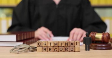 Resmi bir mahkeme salonunda, yargıç, yasal kitaplar ve tokmakla çevrelenmiş bir suç kaydını ayrıntılı bir şekilde inceler. Kararları beklerken gerginlik havayı dolduruyor..