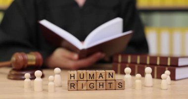 Sakin ve odaklanmış bir ortamda, birisi açık bir kitabı incelerken ahşap figürler masadaki insan hakları kelimelerini çevrelemektedir. Bu ayar hukuk eğitiminin önemini vurgular.