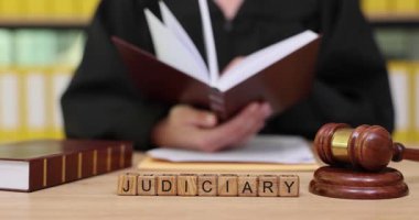 Parlak bir kütüphanede, birileri yasal metinleri dikkatle ve dikkatle inceler. Tokmak, yargı sistemindeki otorite ve düzeni sembolize ediyor. Bilgi derinleştikçe sayfalar dönüyor.
