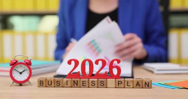 Parlak bir çalışma alanında, bir kişi belgeleri gözden geçirir ve 2026 hedeflerini özetler. Dikkatle, başarı için yeni fikirler ve stratejilerle dolu bir iş planı hazırlıyorlar..