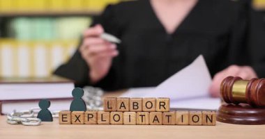 Siyahlar içindeki bir kişi, yasal semboller ve işgücü sömürüsüyle ilgili kelimelerle dolu bir masanın üzerindeki belgeleri inceliyor. Düşünceli tavırları ciddi meseleleri yansıtıyor..