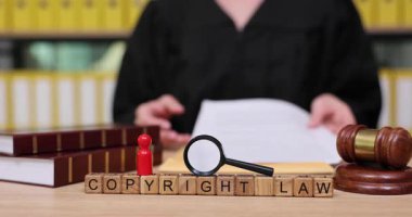 Bilge bir kişi yasal kitaplar ve araçlarla çevriliyken telif hakkı hukukunu tartışır. Kilit kavramları bilgilendirici bir şekilde netleştirmek için bloklar ve bir büyüteç kullanıyorlar..