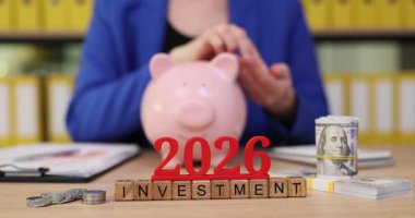 Parlak bir ofiste, eller bir kumbaraya bağlanır, yatırım ve tasarruf planlarını tartışırlar. Parlak renkli görseller 2026 yılı için stratejileri vurguluyor ve finansal büyümeye ilham veriyor.