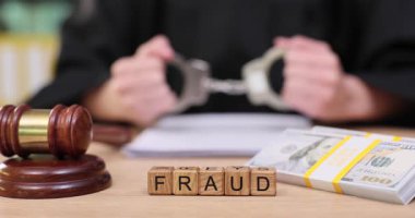 Ciddi bir mahkeme salonunda yargıç sahtekarlıkla ilgili evrakları gözden geçirir. Kelepçeler, suç için adalet aranırken durumun ciddiyetini simgeliyor..