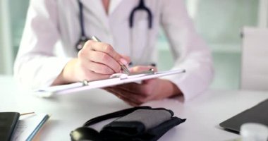 Kadın doktor hasta muayenesinin sonuçlarını dikkatlice panoya kaydediyor. Beyaz önlüklü doktor gerekli ilaçlar için reçete yazıyor.