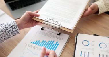 Tecrübeli iş kadını gözden geçirilmesi için ortağına kontrat sunar. İşadamı masasında oturuyor ve detaylara dikkat ederek yükümlülükleri ve şartları çalışıyor.