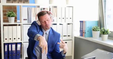 Kulaklık takan ofis çalışanı laptopun yanında oturmuş enerjik hareketler yapıyor. Dans eden ve el sallayan adam, başını sallayarak ritmin tadını çıkarıyor.